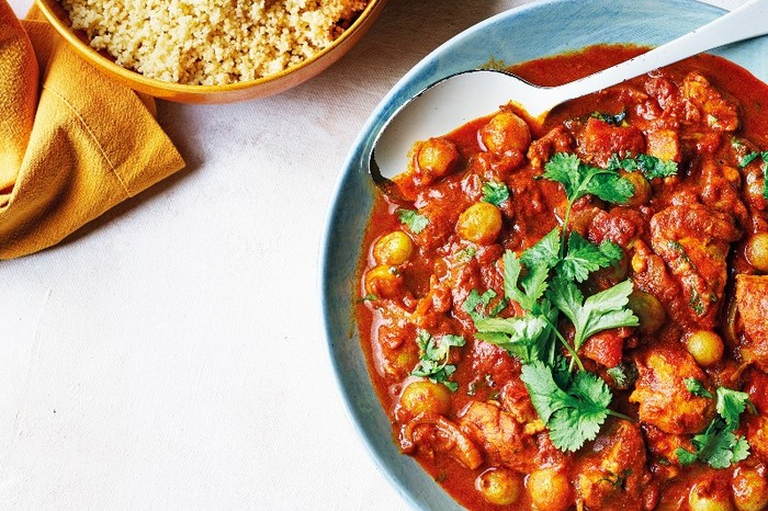 a blue bowl filled with a red tagine with chunks of chicken and gooseberries next to a bowl of couscous