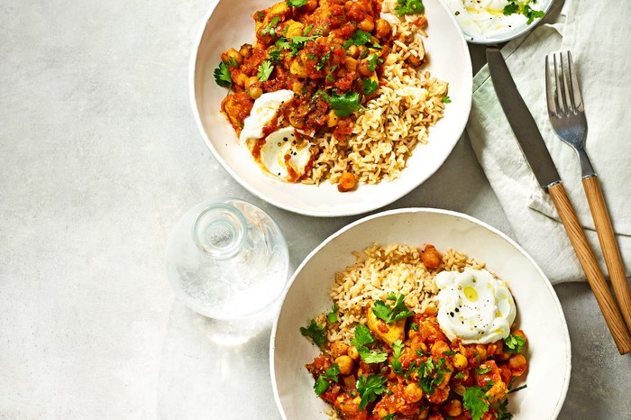 Two bowls of chicken curry with a white linen napkin and wooden-handled cutlery