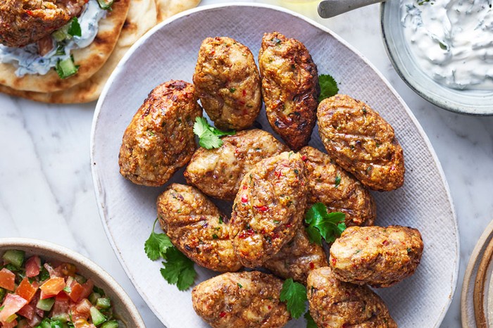 Serving bowl of chicken kofta next to flatbreads, salad and dip