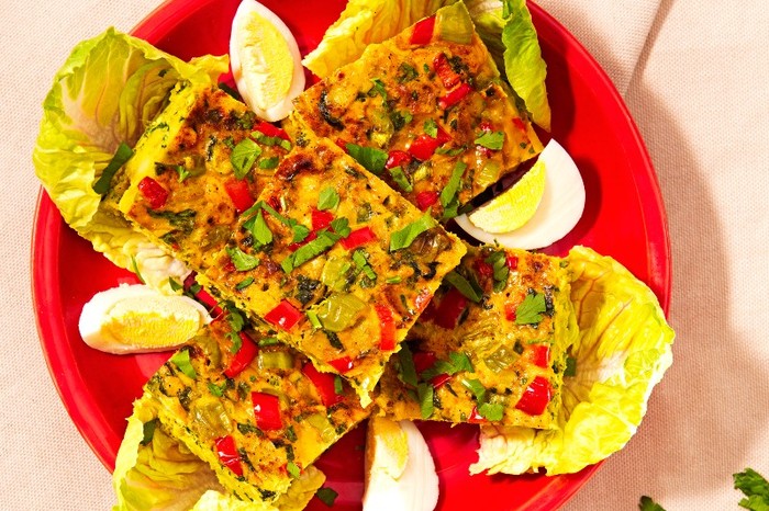 a red plate filled with squares of chicken tajin topped with herbs and a quartered boiled egg alongside