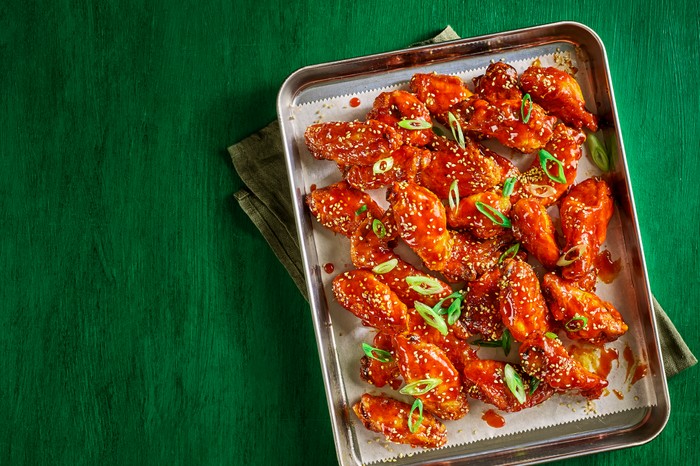 A baking tray filled with chilli sauce-glazed chicken wings and sprinkled with sesame seeds