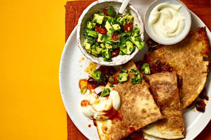 a white plate of quesadillas, guag and sour cream on a red cloth with an orange background