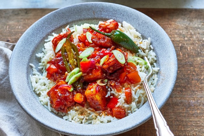 A bowl of chilli paneer fry with a silver spoon on a wooden table