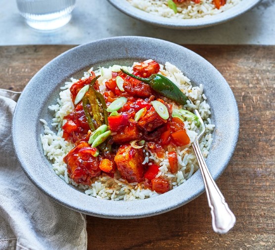 A bowl of chilli paneer fry with a silver spoon on a wooden table