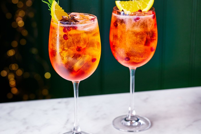 Two wine glasses filled with orange festive-flavoured spritz garnished with orange, star anise and pomegranate seeds