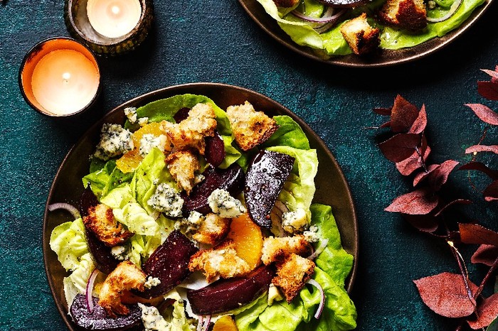 A Citrus, beetroot and blue cheese panzanella salad on a brown bowl with a green background