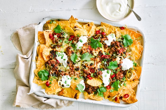 A tray of nachos topped with minced beef, chilli and cheese next to a pot of soured cream