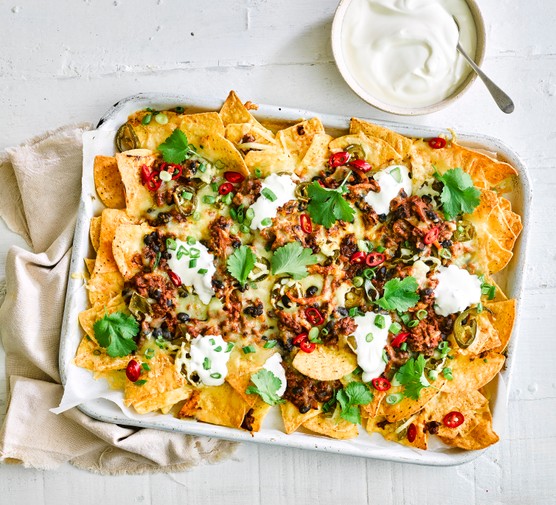 A tray of nachos topped with minced beef, chilli and cheese next to a pot of soured cream