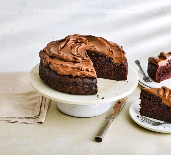 chocolate cake topped with chocolate frosting on a ceramic cake stand with a slice cut out of the middle