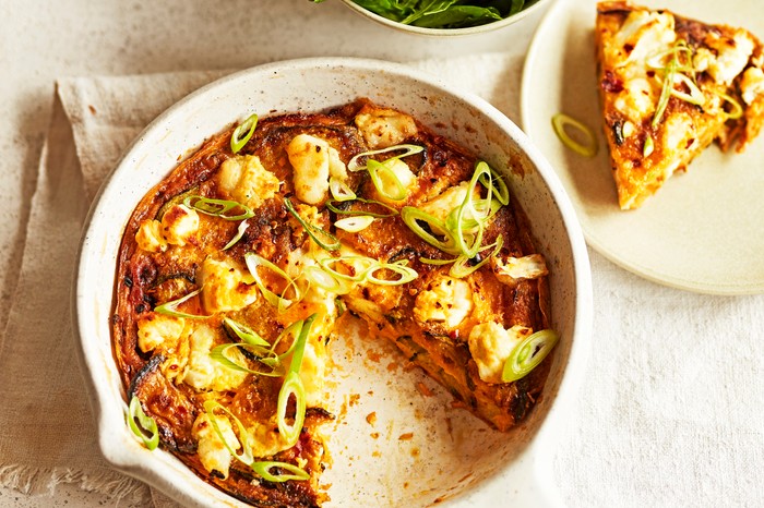 Courgette frittata with a slice cut out presented on a table with a green leafy salad