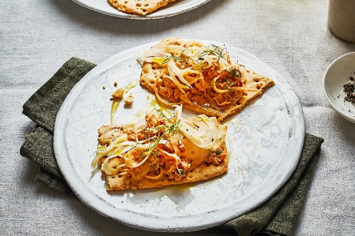 Two crisp breads on a white plate topped with crabmeat and fennel