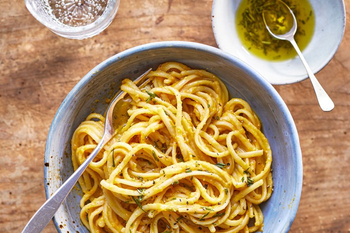 Bowl of spaghetti with butternut squash sauce next to bowl of oil and glass of water