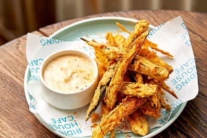 A blue and white pattered plate with deep fried strips of okra and a small pot of creamy dip on a wooden table