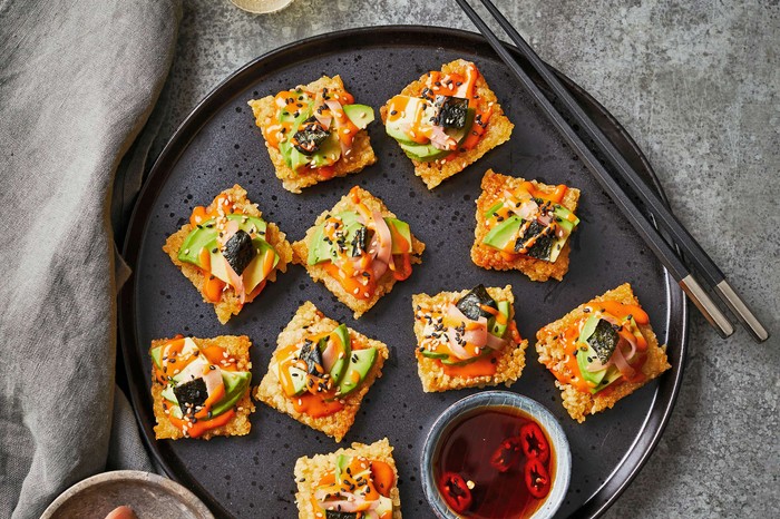 Rice squares topped with sushi on top on a black plate with chopsticks on the side