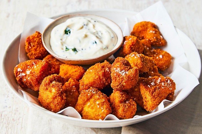 A white platter of nuggets around a pot of white creamy sauce