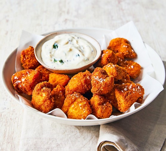 A white platter of nuggets around a pot of white creamy sauce