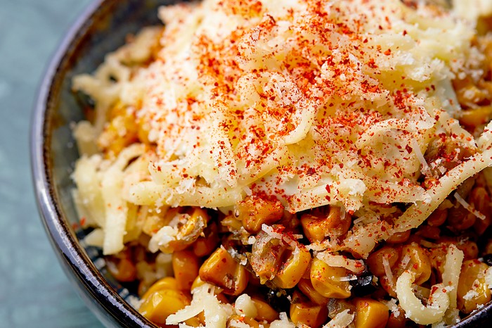 A black bowl filled with sweetcorn and topped with mozzarella cheese and red chilli powder