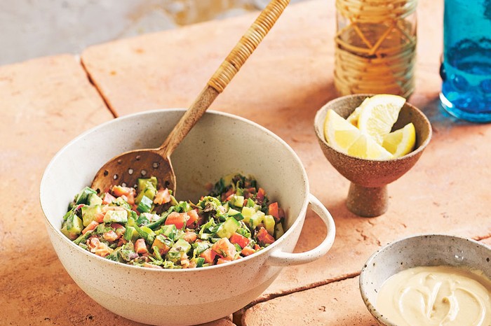 Mixing bowl of Ethiopian salata dakwa salad with a wooden spoon next to a bowl of lemon wedges and dressing