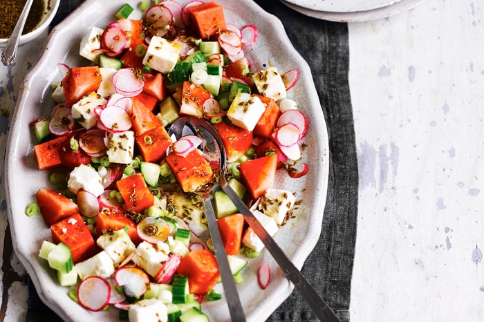 Watermelon and feta salad with a pomegranate dressing served on an oval light coloured serving dish with a salad spoon and fork for serving