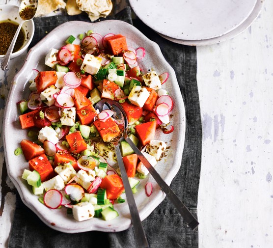 Watermelon and feta salad with a pomegranate dressing served on an oval light coloured serving dish with a salad spoon and fork for serving