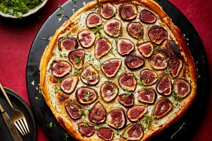 A whole fig tart on a black circular serving platter