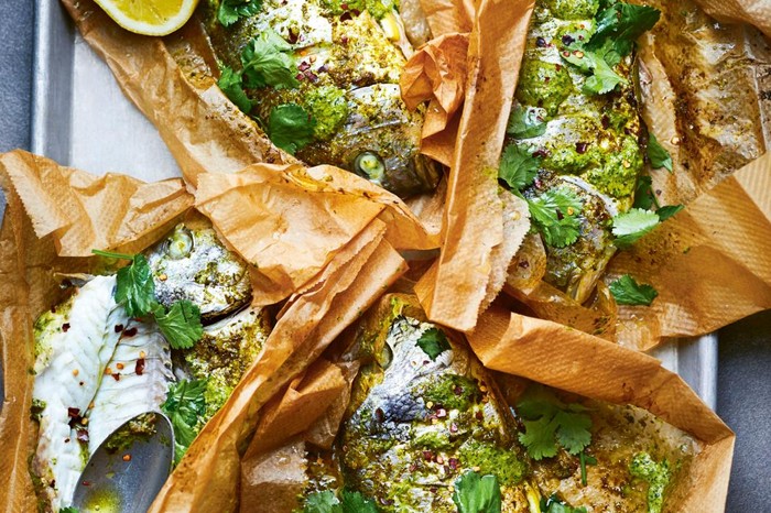 Whole fish wrapped in paper on a silver baking tray