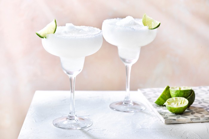 Two frozen margaritas with lime wedges in the background