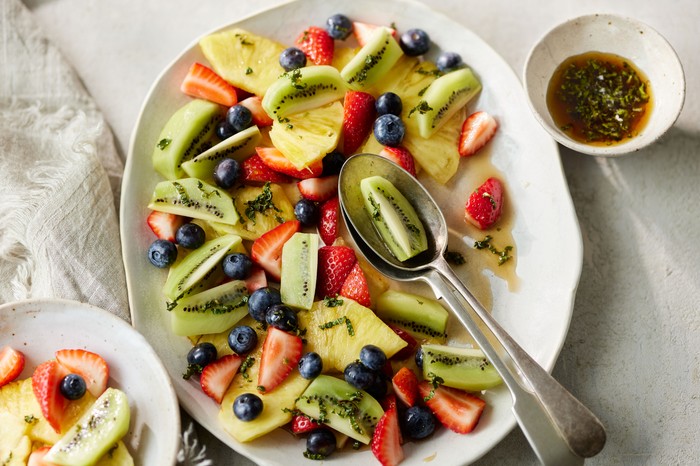 A white bowl of fruit salad including kiwi, blueberries and strawberries