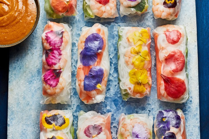 Rows of summer rolls next to a peanut dipping sauce.