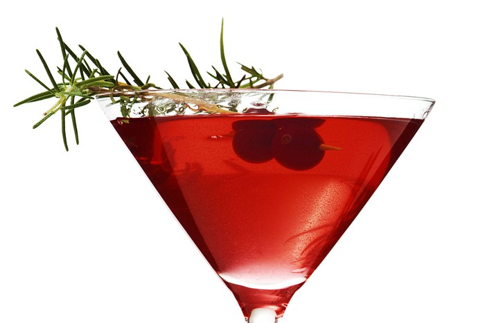 A cocktail glass with a red cocktail in it garnished with rosemary