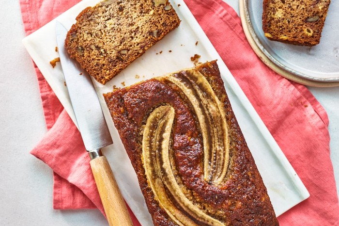 A loaf of banana bread with a banana baked into the top, on a white plate