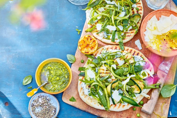 flatbreads spread with ricotta and topped with ricotta and green veg on a wooden board