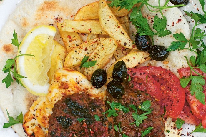 Plate filled with grilled meat patties, sliced tomato and flatbread