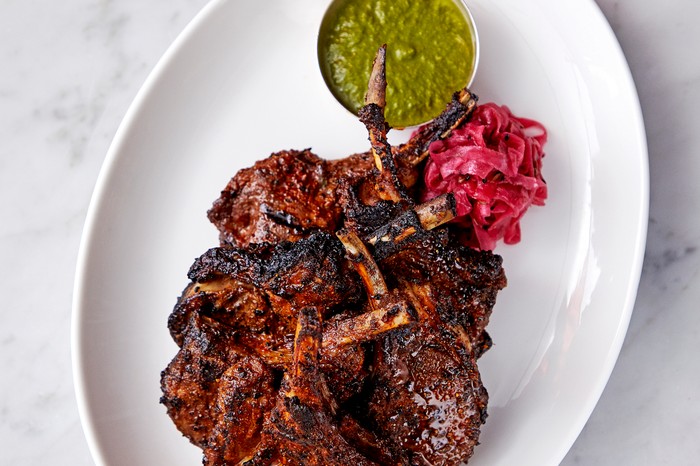 A white plate topped with griddled lamb chops with a side of green chutney