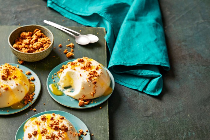 Individual panna cottas on blue plates with sweet crumbs on top