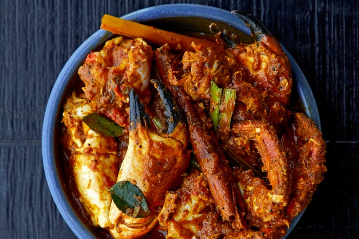 A bowl of crab kari topped with crab claws on a slate background