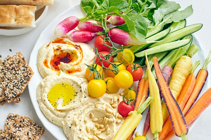 Platter of hummus with an assortment of vegetables next to savoury biscuits and focaccia slices.