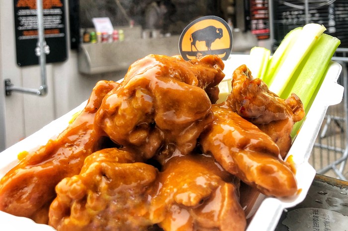 A takeaway plate filled with buffalo wings and sticks of celery