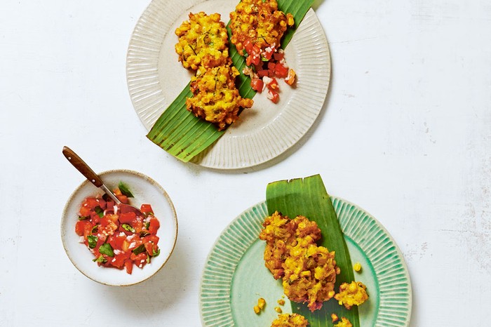 Two plates of sweetcorn fritters next to a bowl of chilli and tomato sambal.