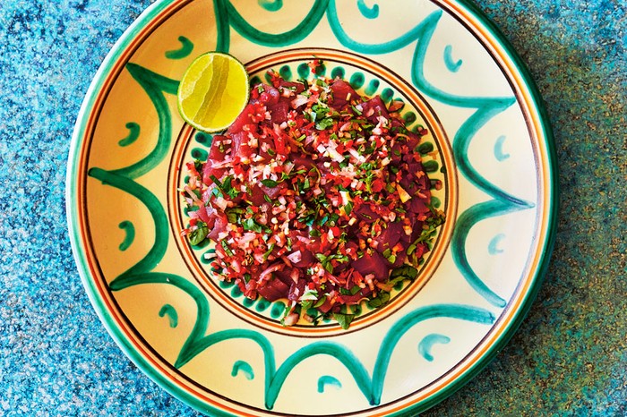 Bowl of small chunks of raw tuna with chillies and tomatoes, next to a lime half.