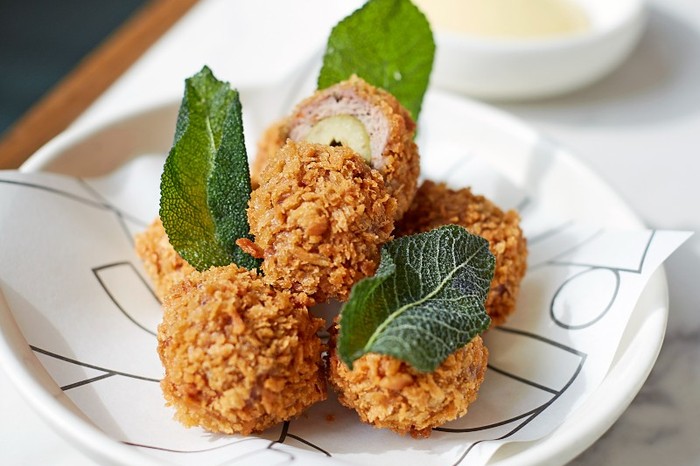 A plate of olives coated in golden breadcrumbs with fresh herbs