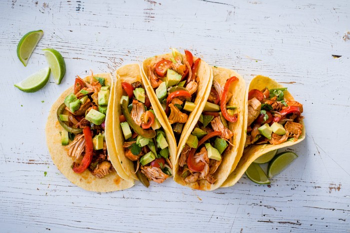 Five jackfruit tacos containing avocado and homemade tomato salsa with lime wedges on the side