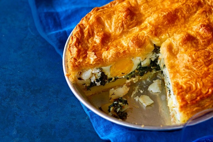 Smoked haddock pie in a pie dish with a slice taken out, against a royal blue fabric background