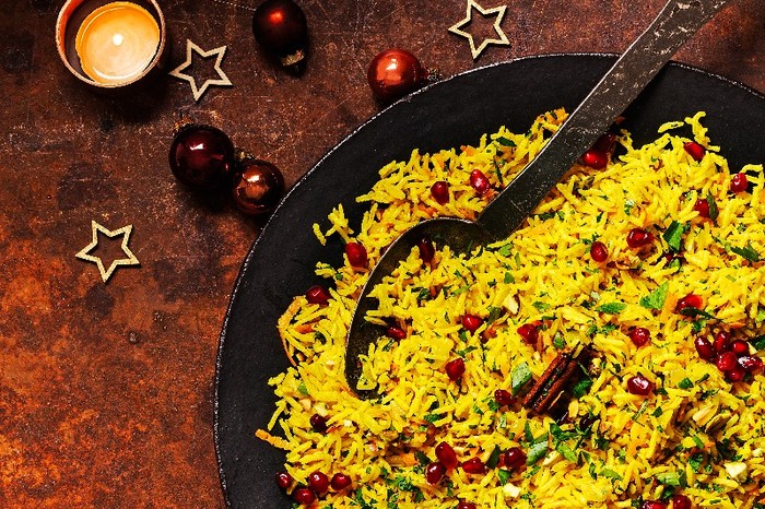 A brown bowl of yellow Jewelled carrot and pistachio pilaf with a large serving spoon