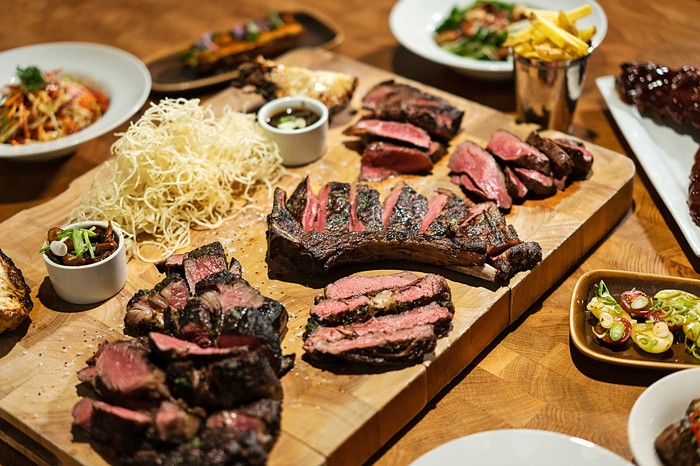 Large cuts of meat on a wooden plank with side dishes such as chips