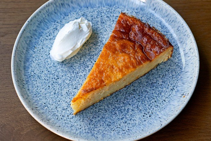 A light blue speckled plate topped with a slice of orange cake, with a quenelle of yogurt on the side