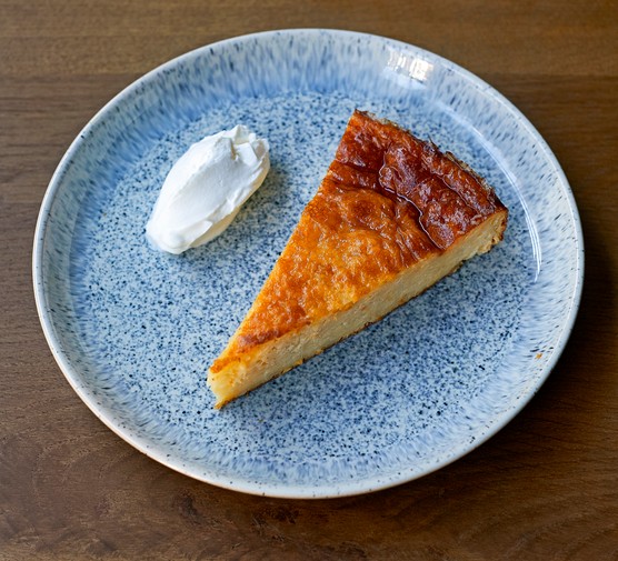 A light blue speckled plate topped with a slice of orange cake, with a quenelle of yogurt on the side