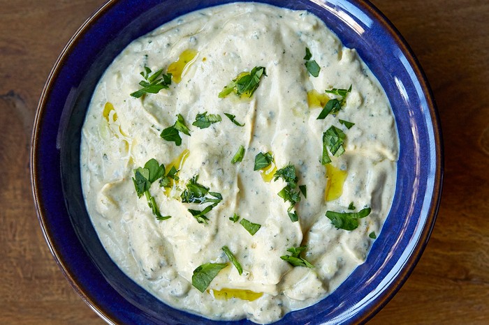 A blue bowl filled with a yogurt and cucumber dip