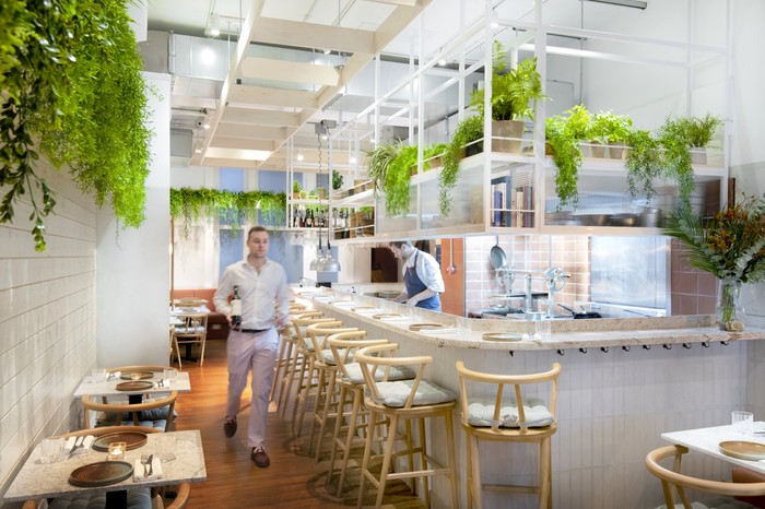 A white dining room with a central bar and greenery cascading down the wallw