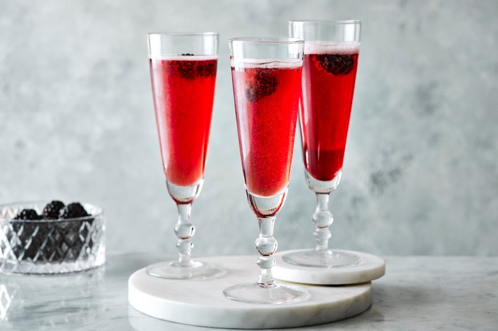 Three kir royale cocktails with blackberries in the background